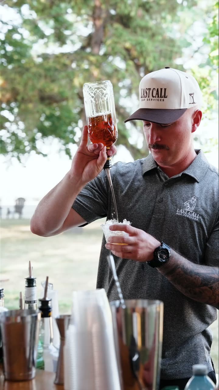 A Last Call bartender in a branded cap building a cocktail