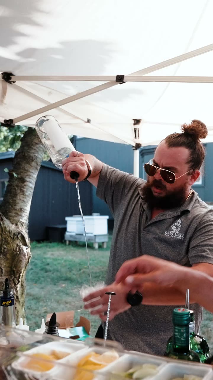 Pouring a drink at a wooden bar under a white tent